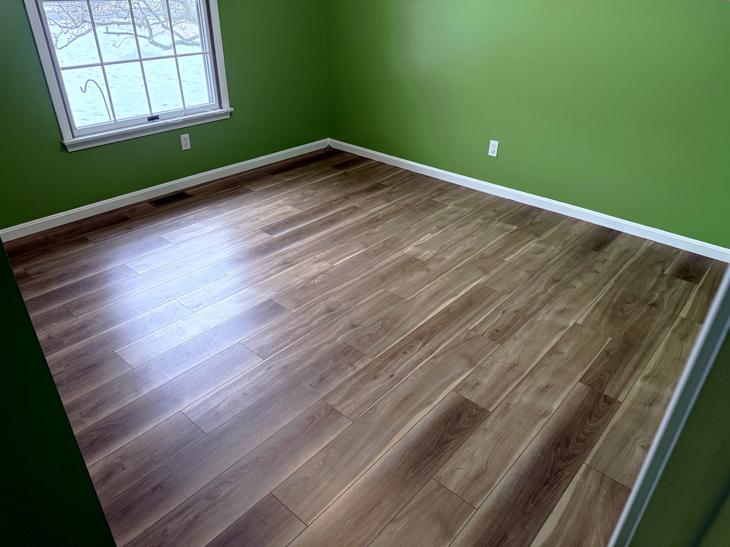 Finished flooring in a room with green walls and white trim