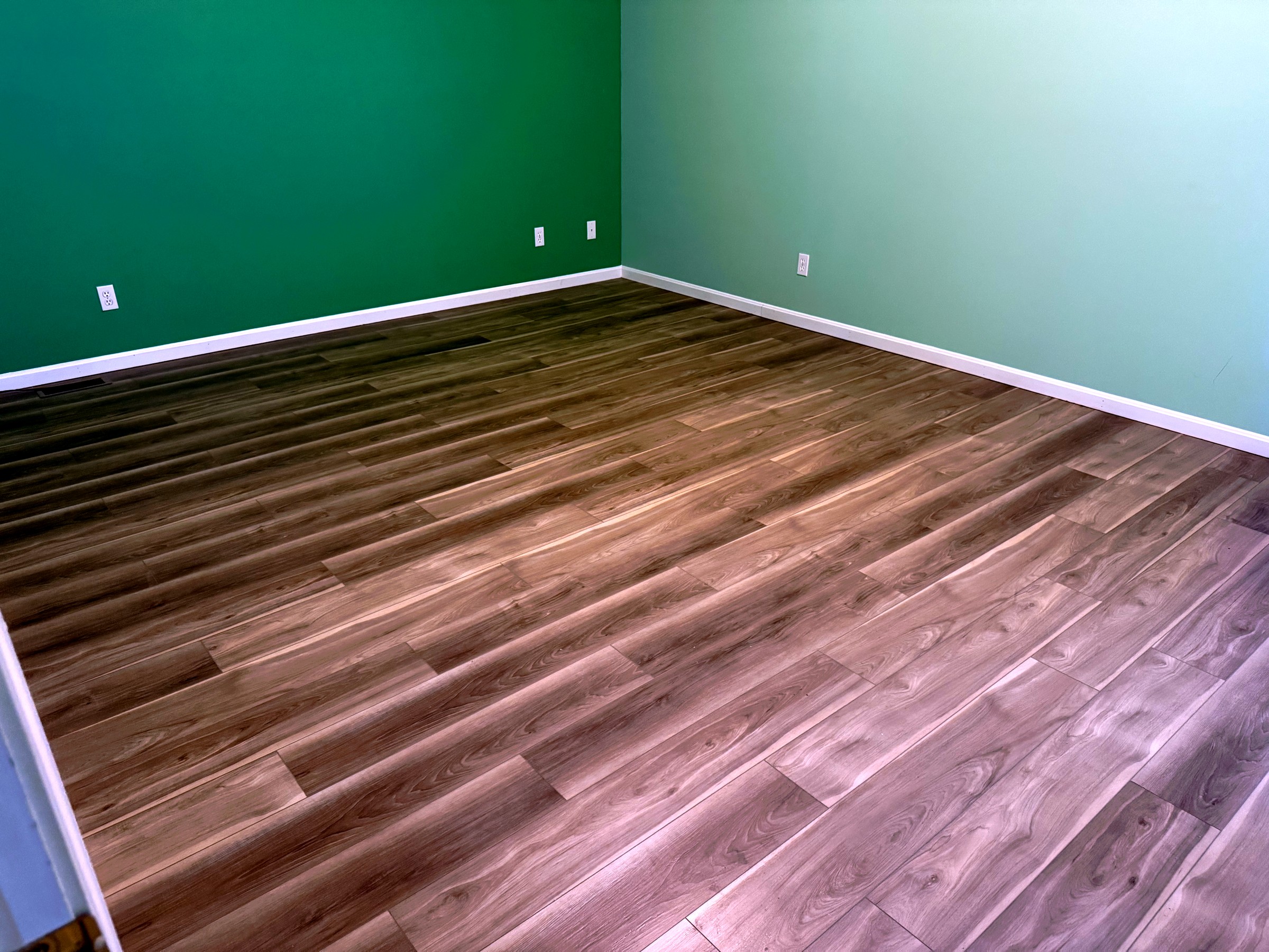 Wide view of finished flooring in a room with two shades of green walls